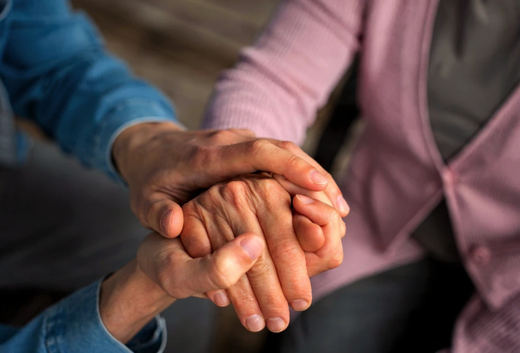 Nurse Or Home Caregiver And Senior Woman Holding Hands At Home